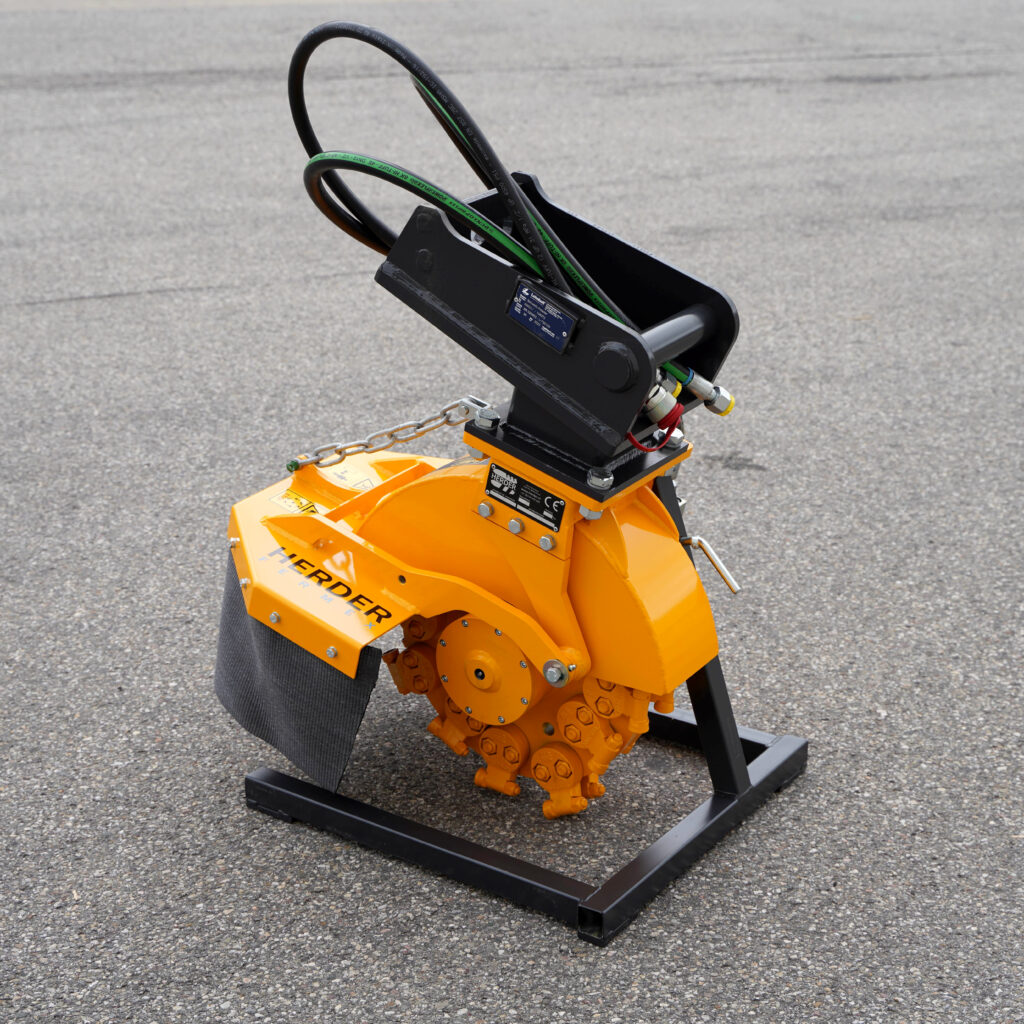 Gelb-schwarzer Stubbenfräse SCE-410H-6 von HERDER mit Hydraulikschläuchen und massiver Stahlkonstruktion steht auf Asphalt im Freien.