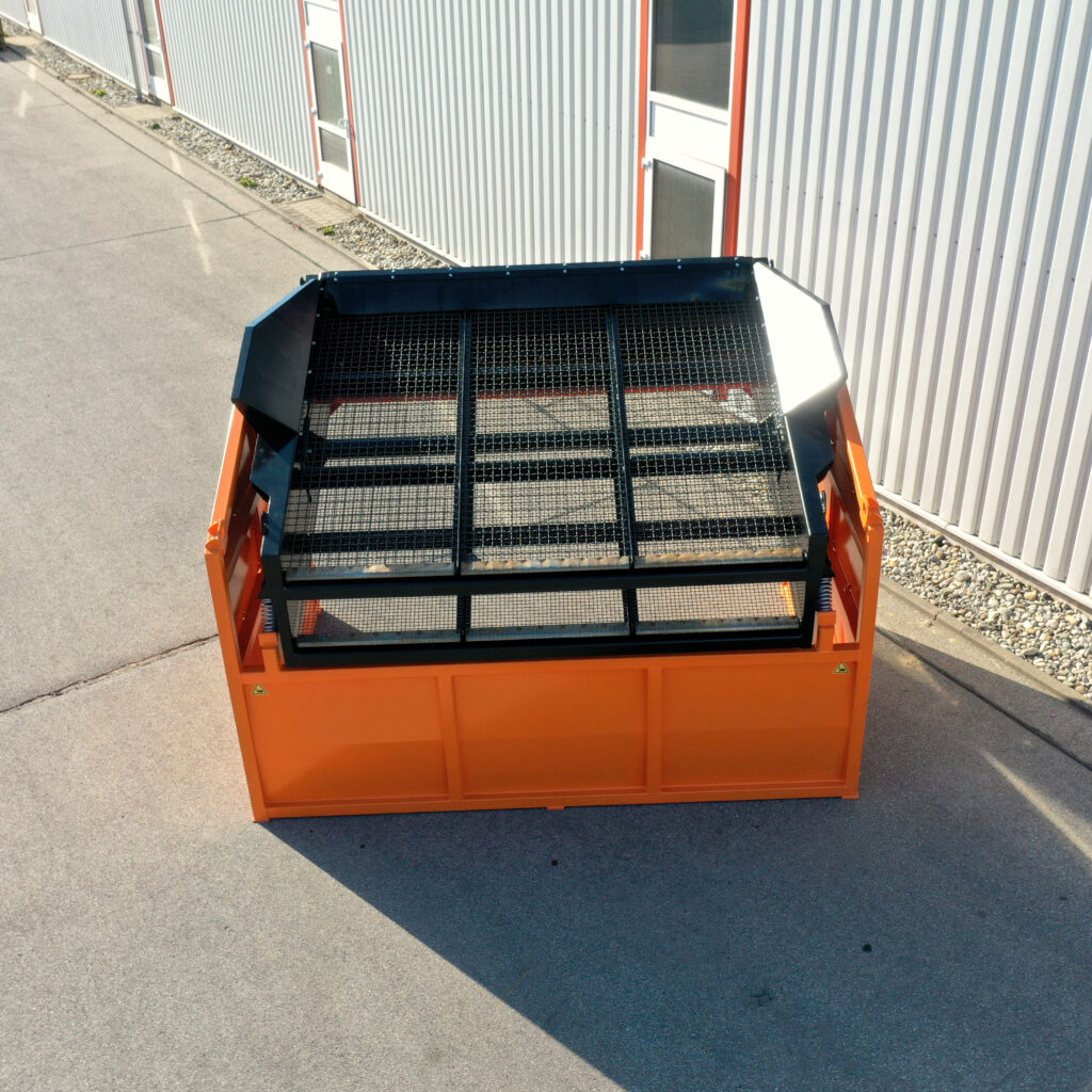 Ein orange-schwarzer Traserscreen DB-50-2 mit feinem Gitteraufsatz steht auf dem Asphalt vor einer hellen Metallhalle in der Sonne.