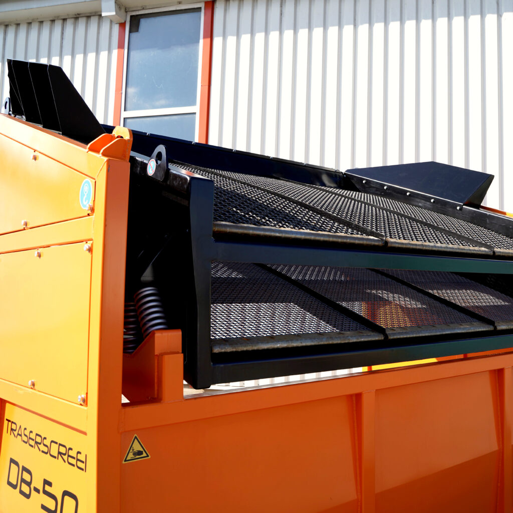 Die orange-schwarze Siebmaschine Traserscreen DB-50-5 steht vor einer hellen Hallenwand, mit schräger Förderfläche und Gitterstruktur im Tageslicht.