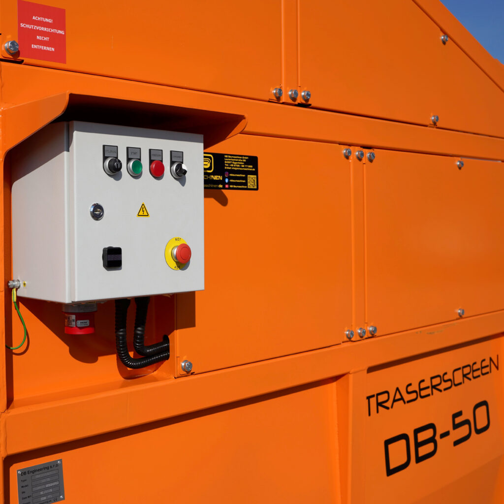 Orange lackierte Traserscreen-Anlage mit weißem Bedienkasten, roten und grünen Tastern sowie Warnhinweisen und sichtbaren Schraubverbindungen im Sonnenlicht.