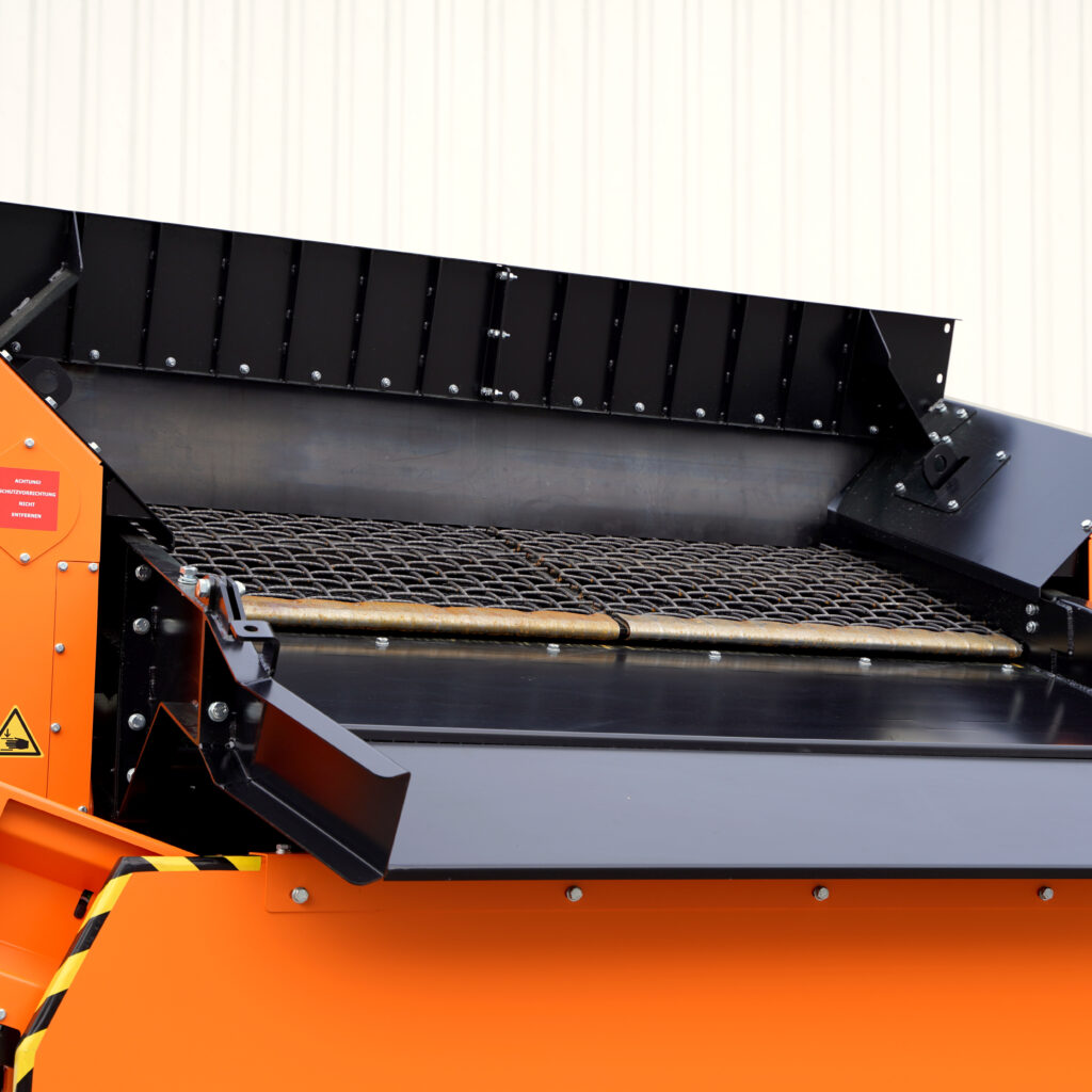Detailansicht eines orange-schwarzen Traserscreen mit verschraubten Blechen, Gitterförderband und Warnhinweisen an der robusten Siebtechnik.