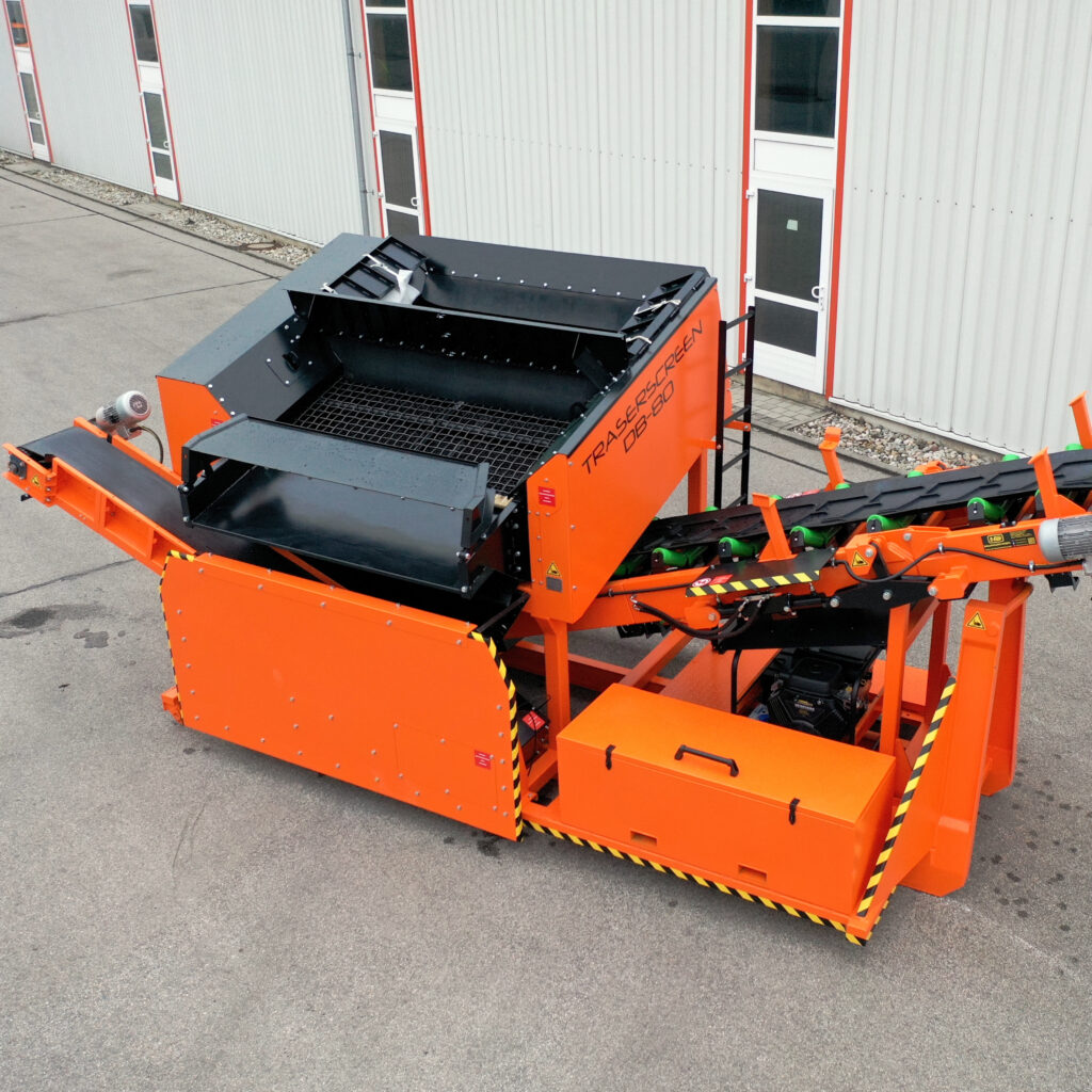 Große Traserscreen DB-80 Siebanlage in Orange und Schwarz steht vor einer hellen Industriehalle, mit Förderband, Gitteraufsatz und robustem Stahlrahmen.