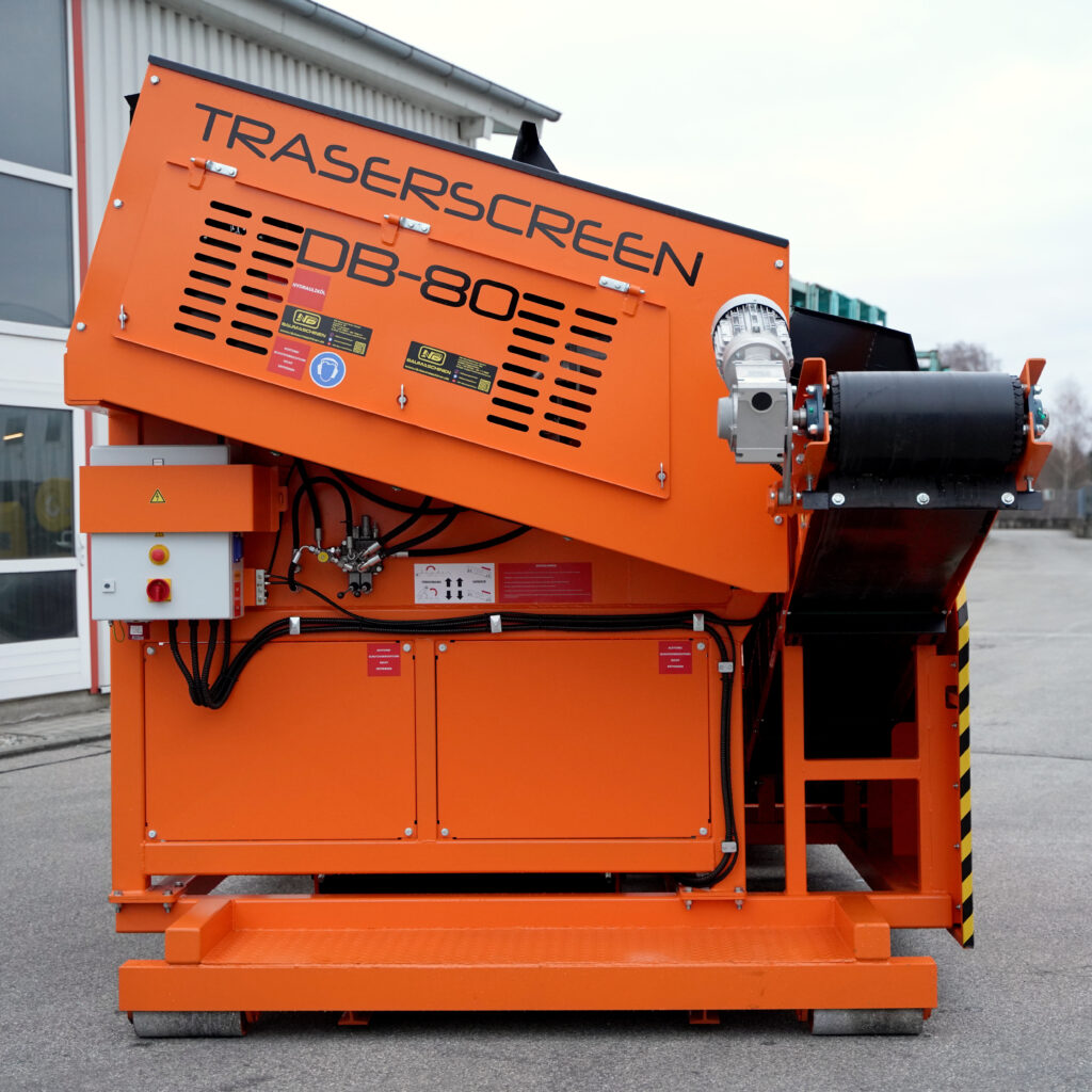 Ein orangefarbener Traserscreen DB-80-6 mit schrägem Gehäuse, Lüftungsschlitzen und schwarzem Förderband steht vor einem Industriegebäude.