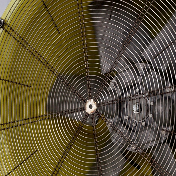 Ein gelber Industrieventilator mit silbernem Schutzgitter und sichtbarer Motoraufnahme füllt den rechten Bildbereich in einer engen Nahaufnahme.