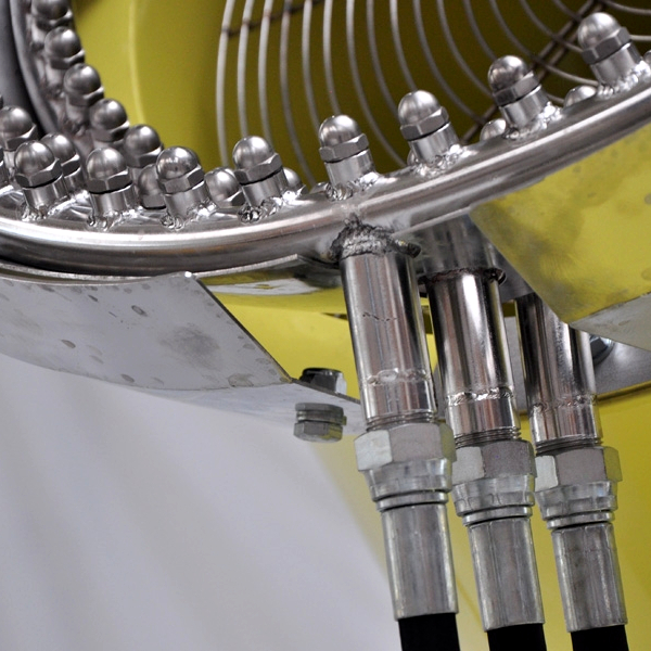 Detailaufnahme eines glänzenden Metallrings mit Schrauben und drei Hydraulikleitungen vor gelbem Maschinengehäuse in einer technischen Anlage.