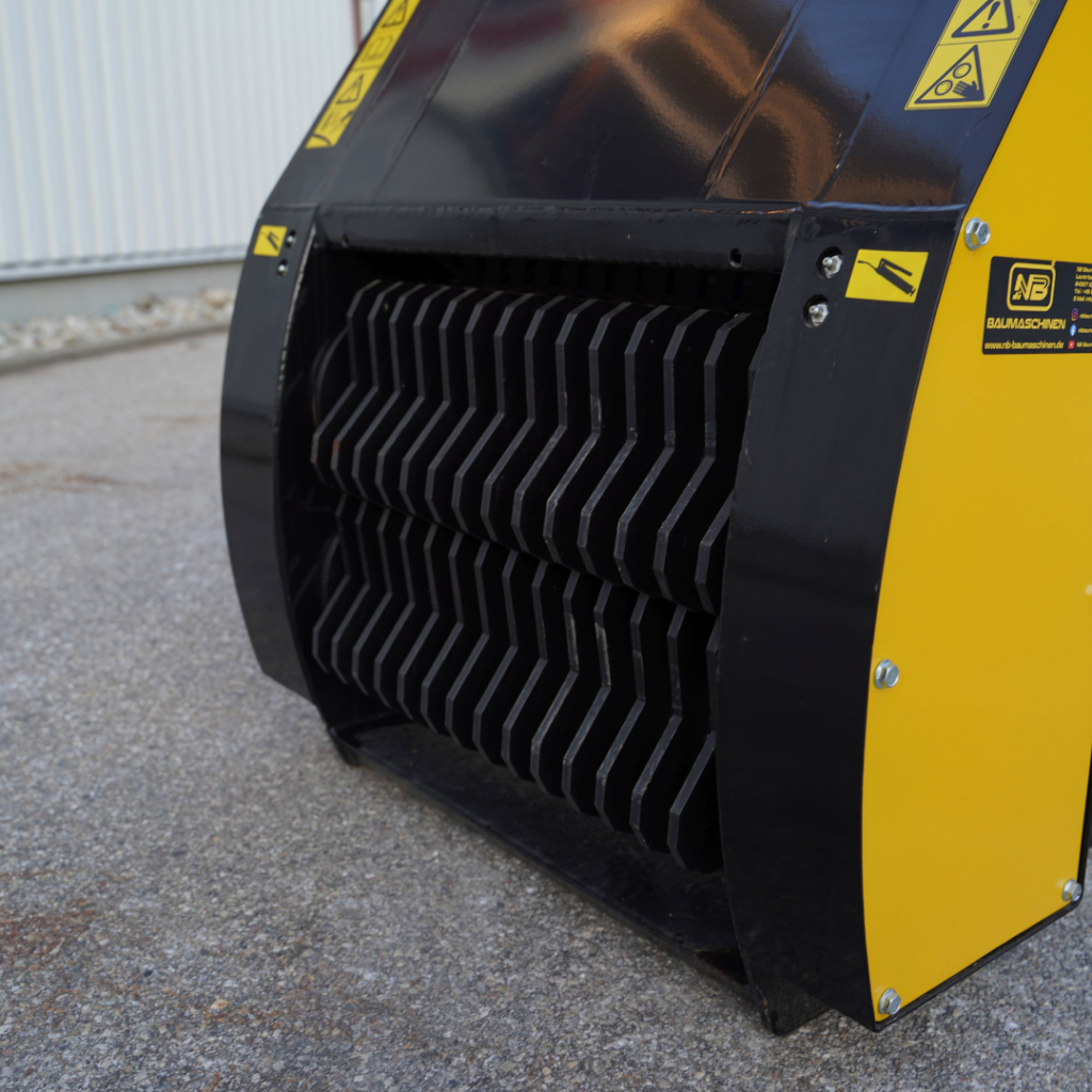 Nahaufnahme eines gelb-schwarzen Recycling-Baumaschinen-Aufsatzes mit zwei massiven Schneidwalzen, Warnsymbolen und robustem Metallgehäuse.