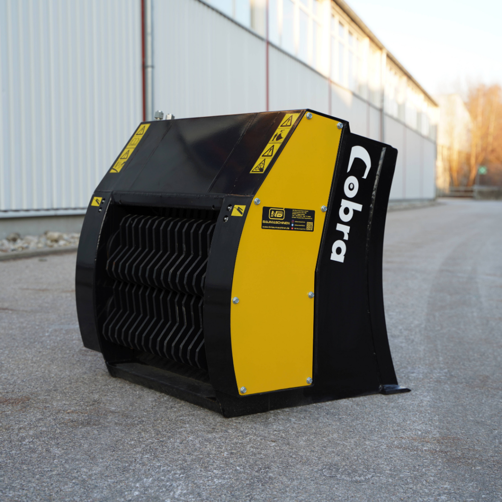 Ein schwarz-gelb lackierter Cobra-Backenbrecher steht auf dem Asphalt vor einer Industriehalle, mit offenem Mahlraum und Warnaufklebern.