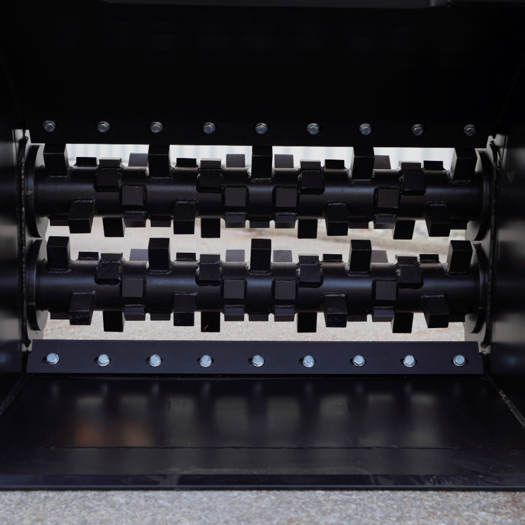 Zwei schwarze, mit kantigen Schneidblöcken besetzte Walzen eines Industriemahlwerks liegen nebeneinander in einem robusten Metallgehäuse mit Schraubreihe.