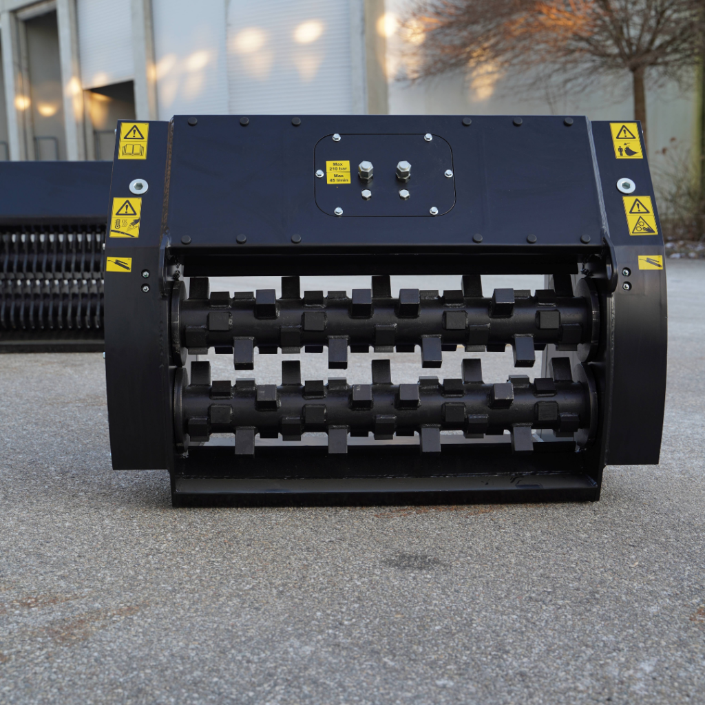Ein schwarzes Maschinenmodul mit zwei gezahnten Walzen und Warnaufklebern steht vor einer Industriehalle auf Asphalt im Freien.