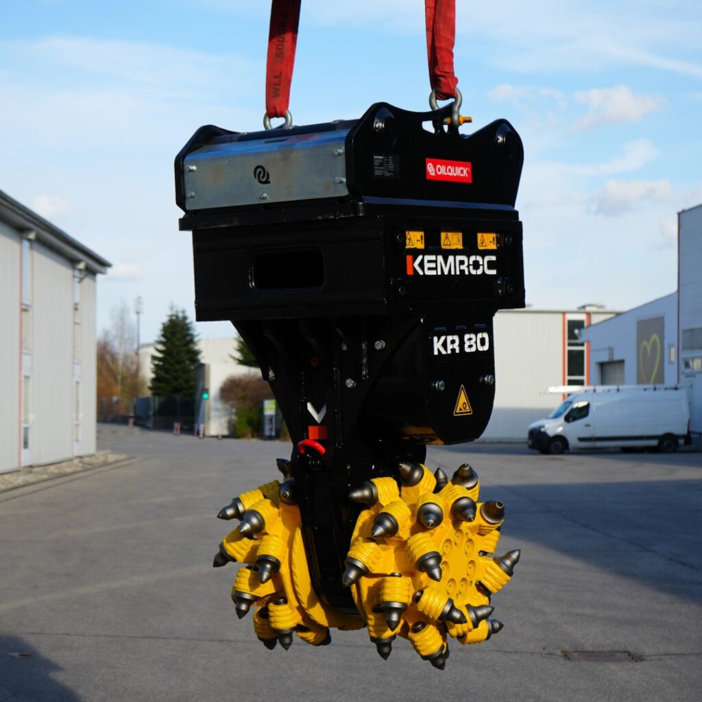 Ein schwarzer KEMROC KR 80 mit gelben Schneidrollen hängt an roten Gurten vor Industriegebäuden, während das Werkzeug frei über dem Asphalt schwebt.