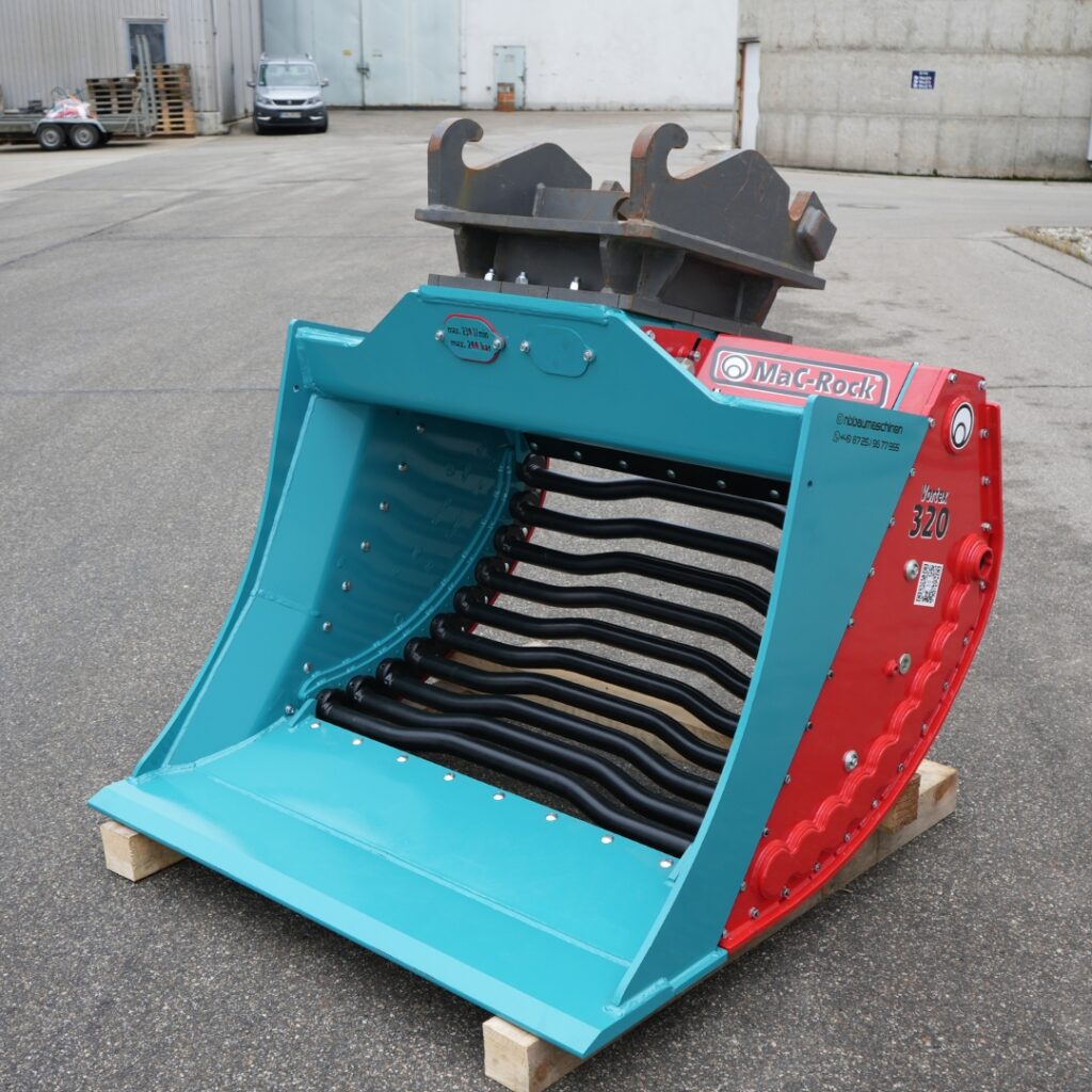 Ein türkis-roter Mac-Rock Vortex 320 mit schwarzen Siebwalzen und schwerem Aufnahmeteil steht auf Holzklötzen im Hof vor einer Industriehalle.