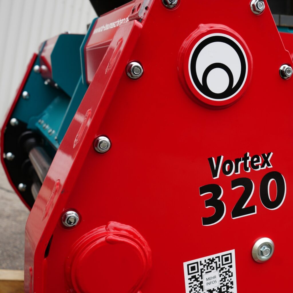 Ein rotes Baumaschinenteil mit der Aufschrift Vortex 320, silbernen Schrauben, einem runden Logo und blauem Maschinengehäuse im Hintergrund.