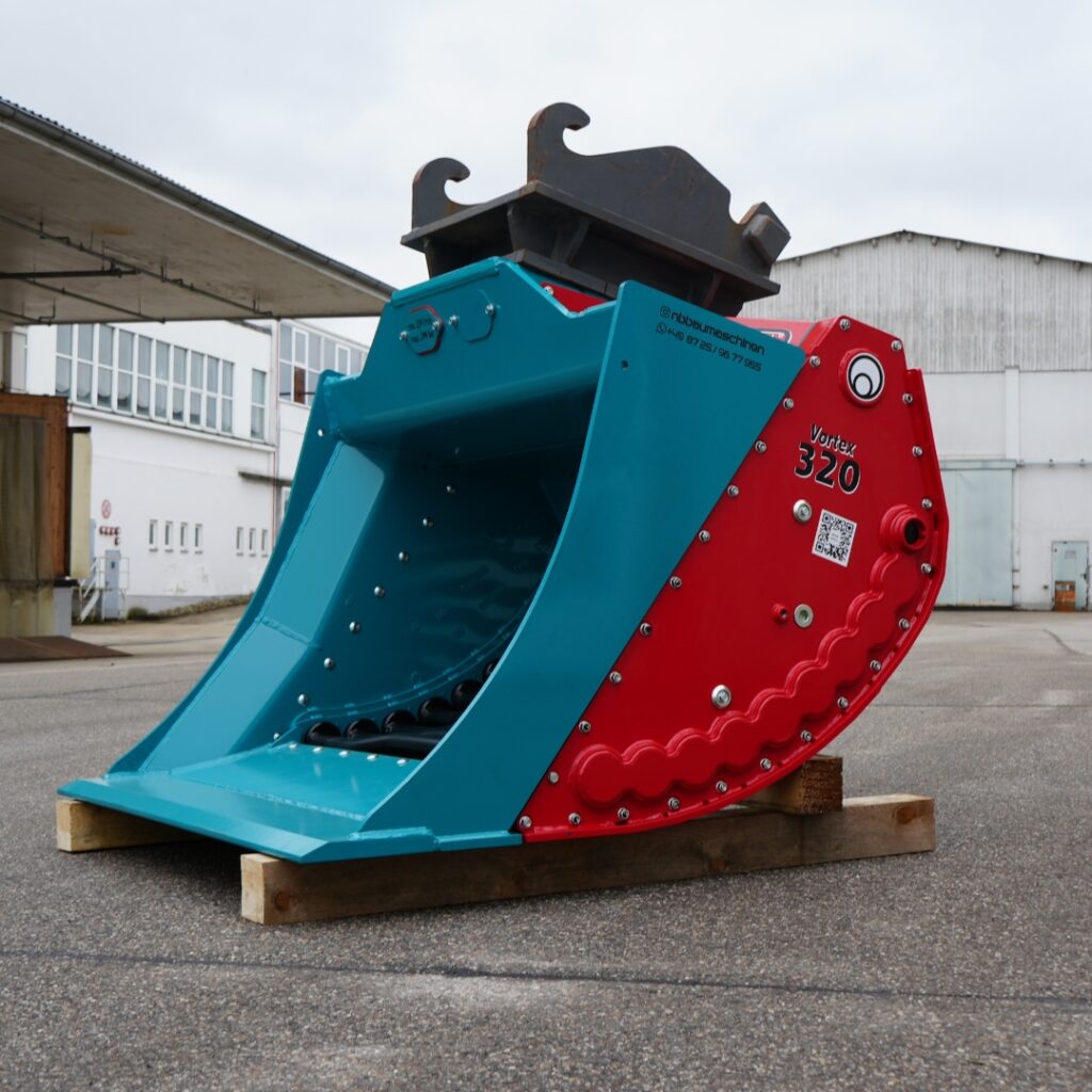 Vor einem Industriegebäude steht ein türkis-roter MacRock Vortex 320 mit schwarzem Aufsatz auf Holzbohlen im Hof, seitlich mit sichtbarer Beschriftung.